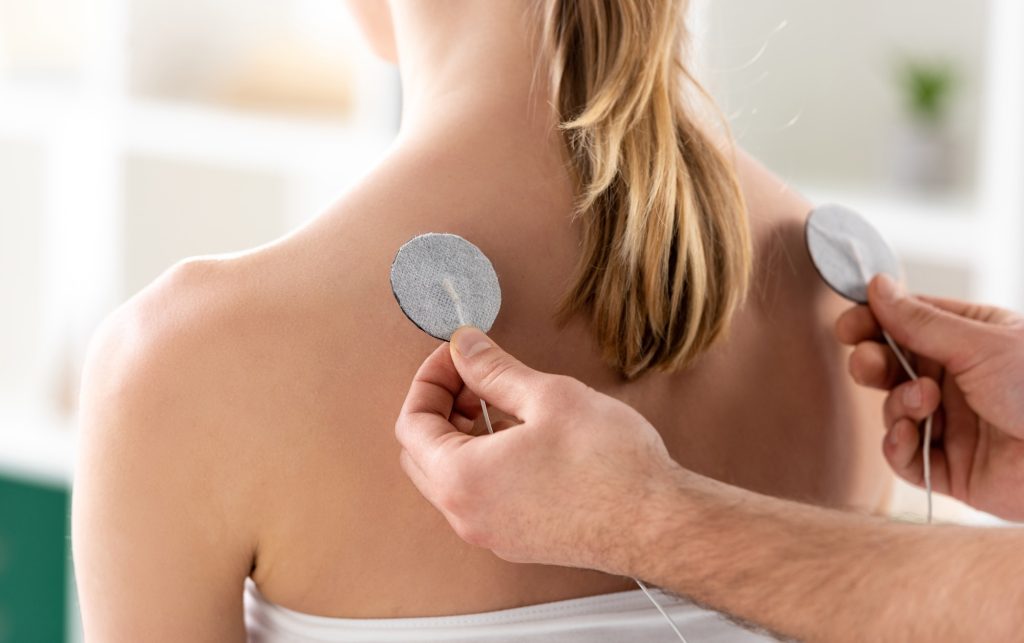 Cropped view of doctor fastening electrodes of patient back during electrotherapy in clinic